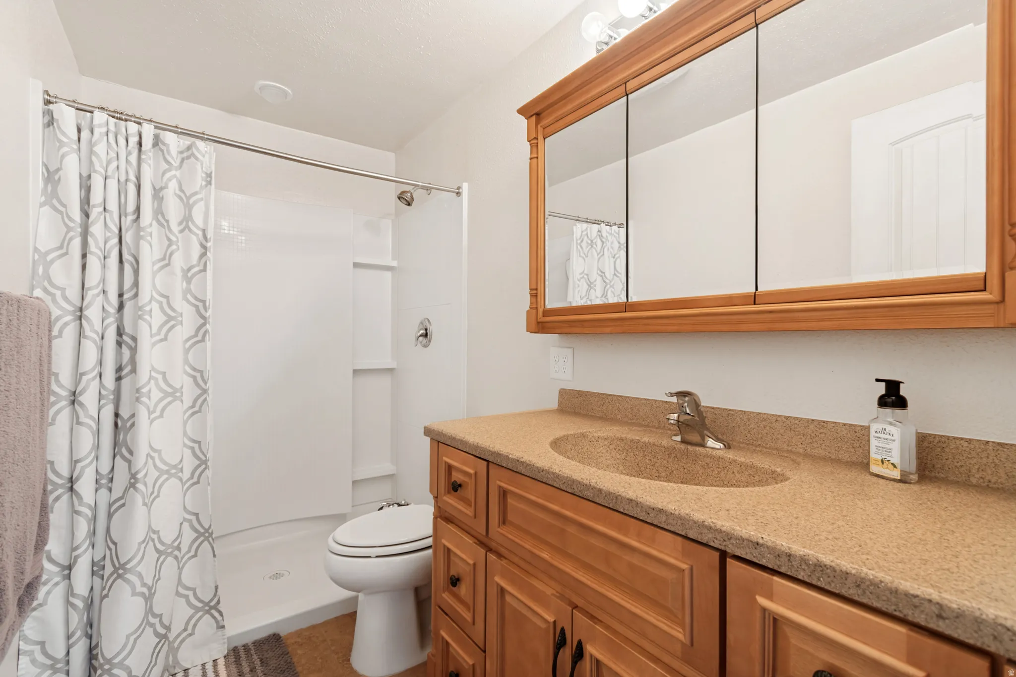 Bathroom featuring a wood-finish vanity with a double sink, stone-finish countertop, and a three-door mirrored medicine cabinet