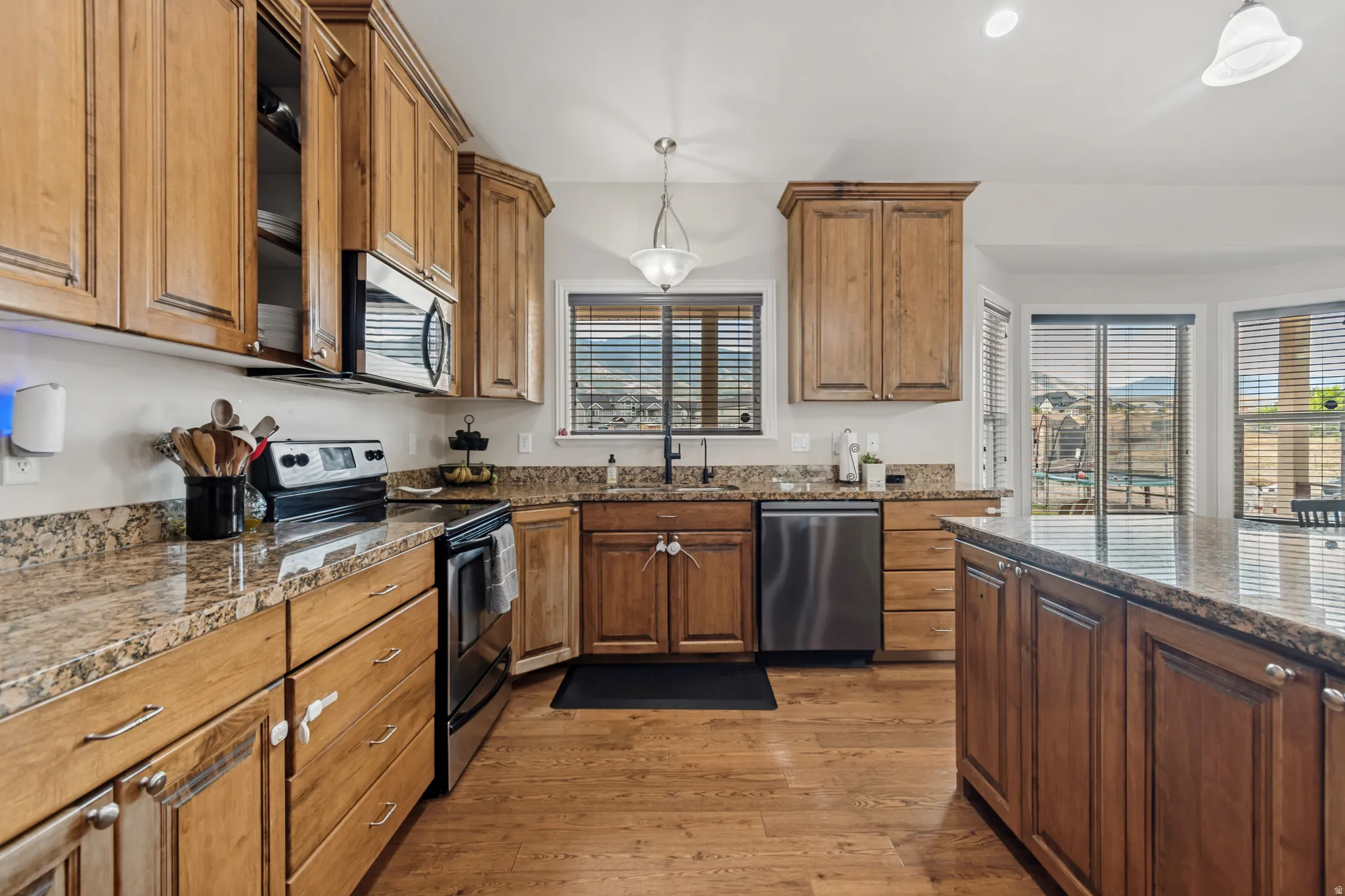 Spacious kitchen featuring natural wood cabinetry, granite countertops, stainless steel appliances, wood-finish flooring, and a large central island
