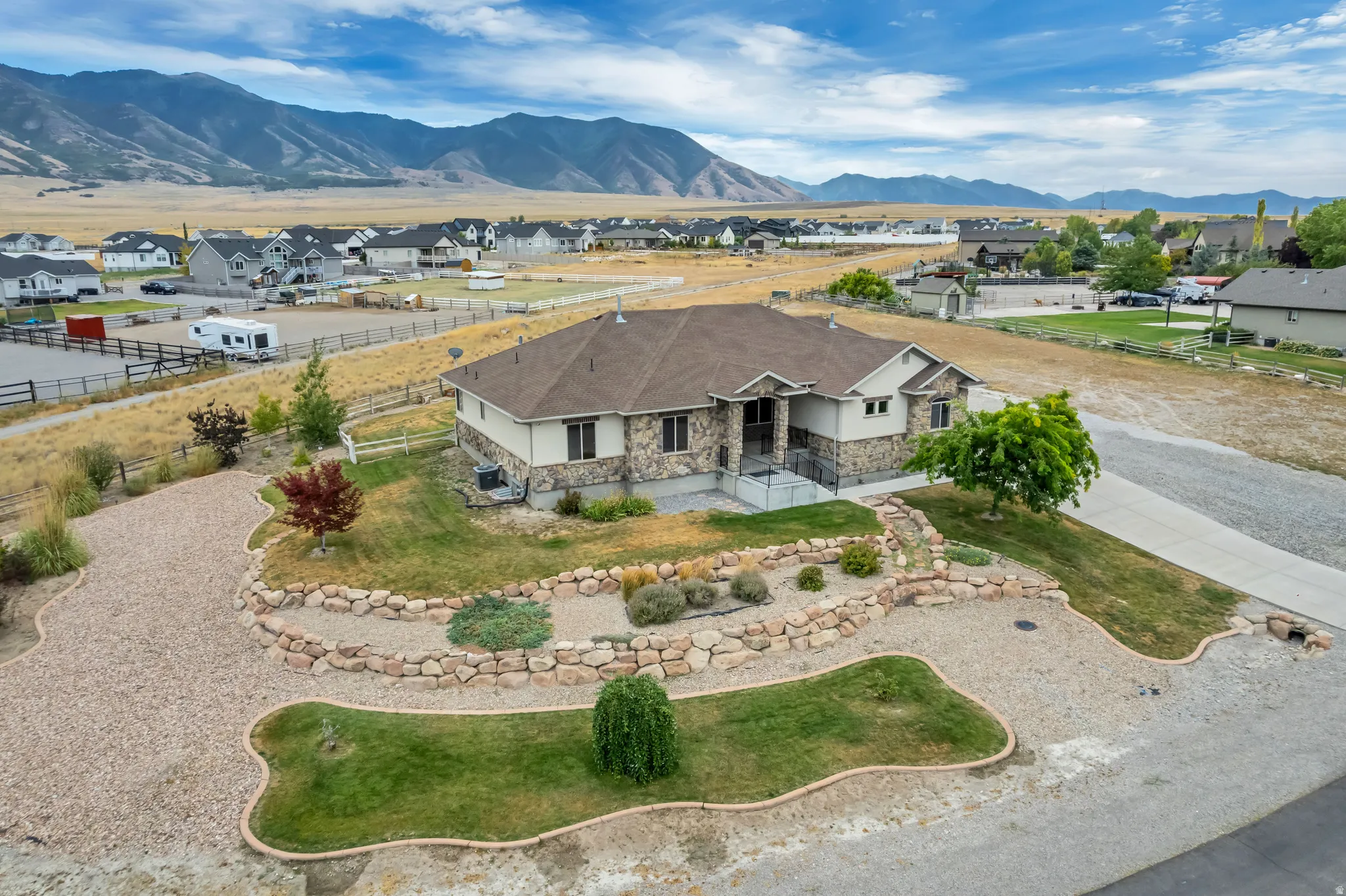 Stone and stucco exterior with a multi-level roofline, featuring a concrete driveway and an additional gravel parking area