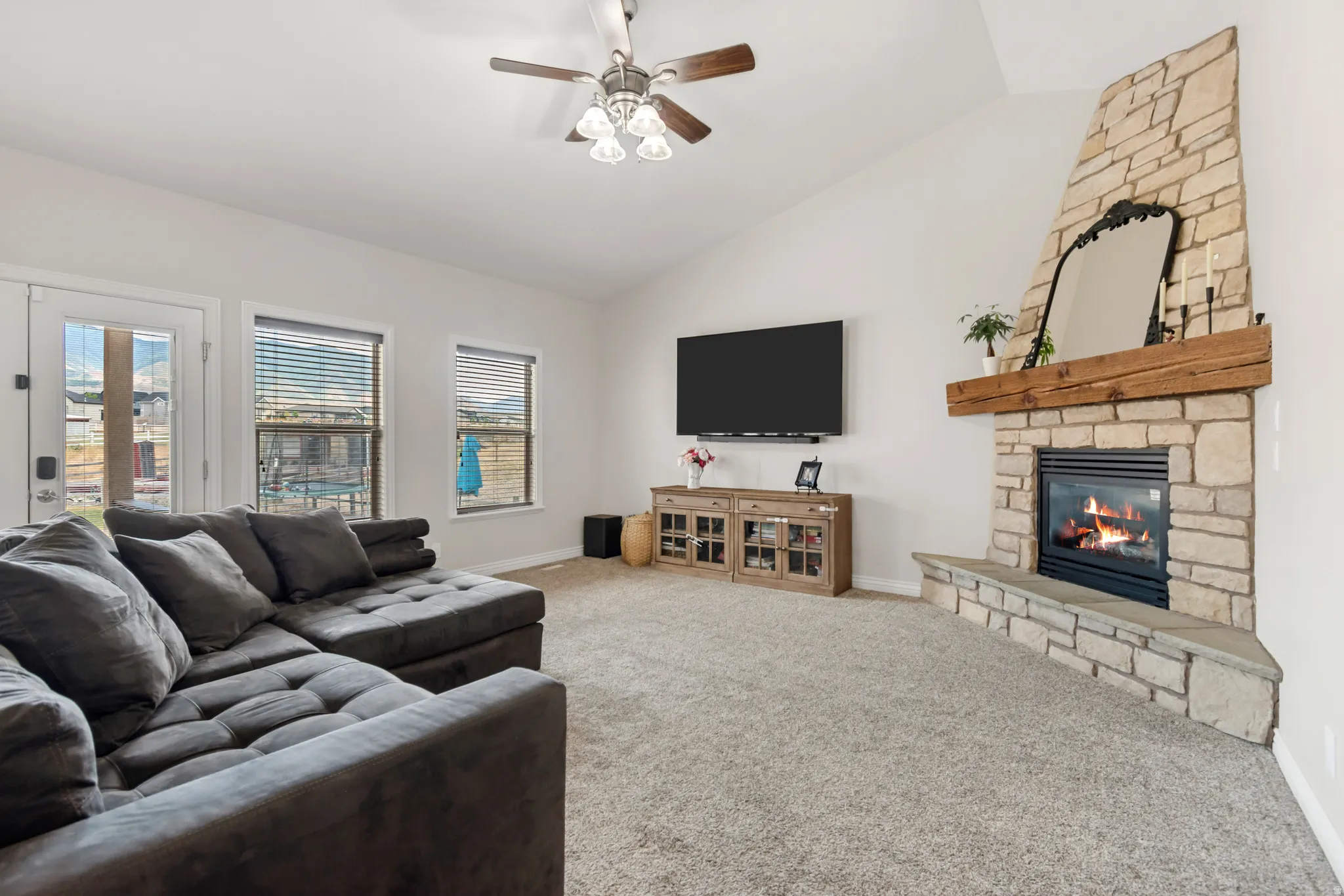 Living area featuring a floor-to-ceiling stone fireplace with a wood mantel, vaulted ceilings, and a ceiling fan