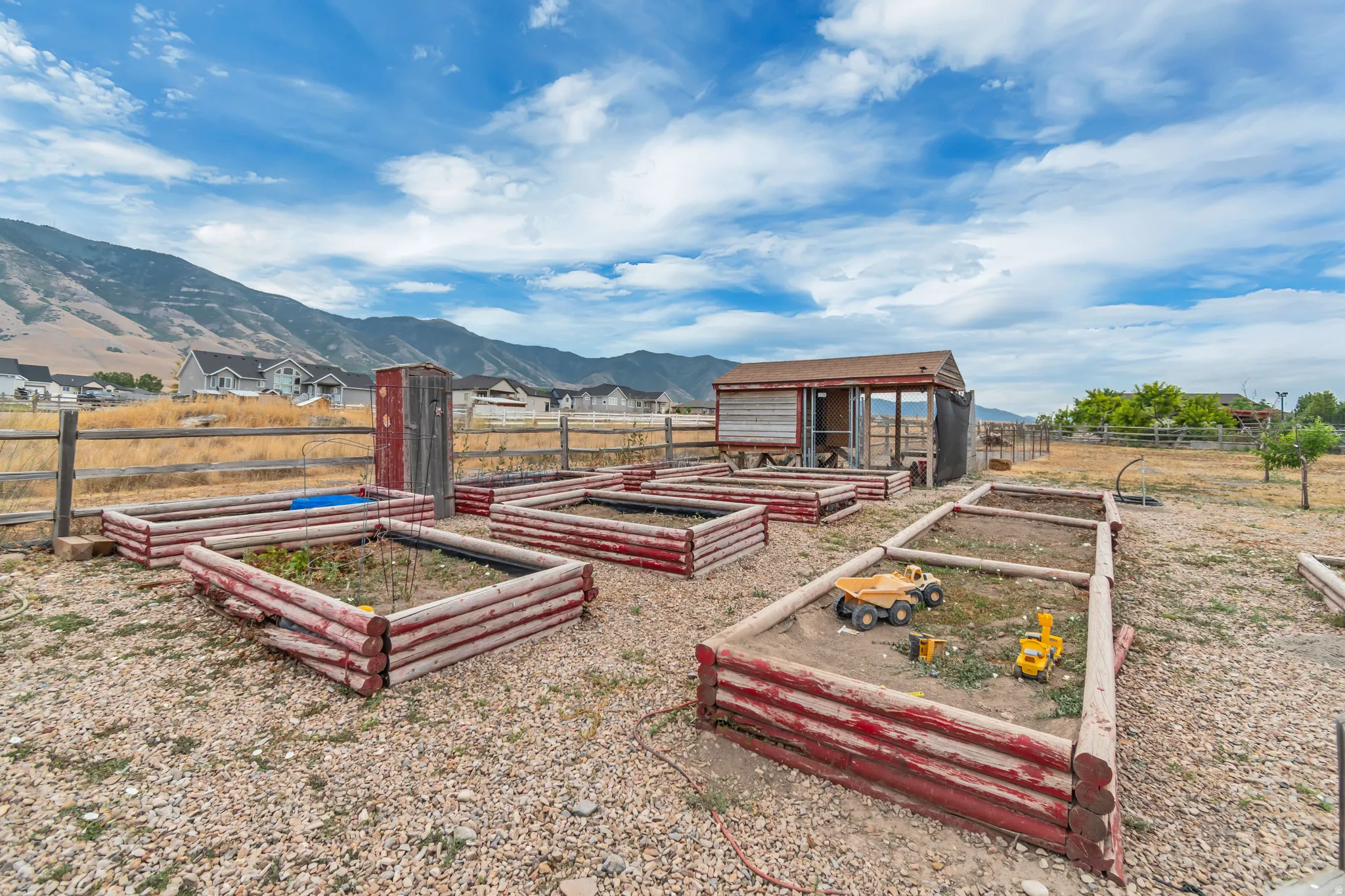 Multiple raised garden beds, a rustic storage shed, and a wooden fence define this outdoor space