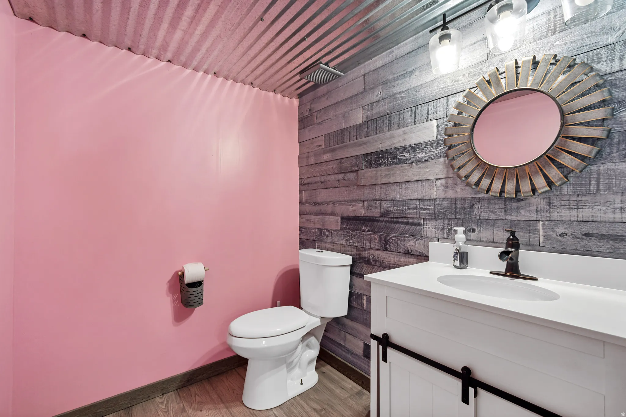 Bathroom featuring corrugated metal ceiling, wood-finish flooring, and a vanity with a white countertop and barn-door style cabinetry