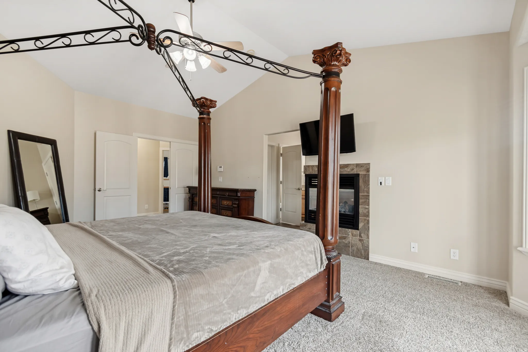 Vaulted ceiling bedroom featuring a fireplace with stone surround, wall-mounted television, and light gray carpet