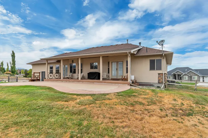 Expansive rear patio area featuring a covered porch, multiple entry points with glass-paneled doors, and a stone accent wall