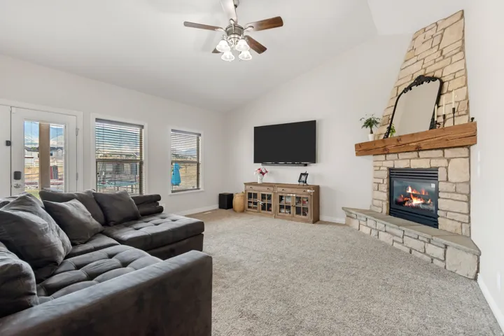 Living area featuring a floor-to-ceiling stone fireplace with a wood mantel, vaulted ceilings, and a ceiling fan