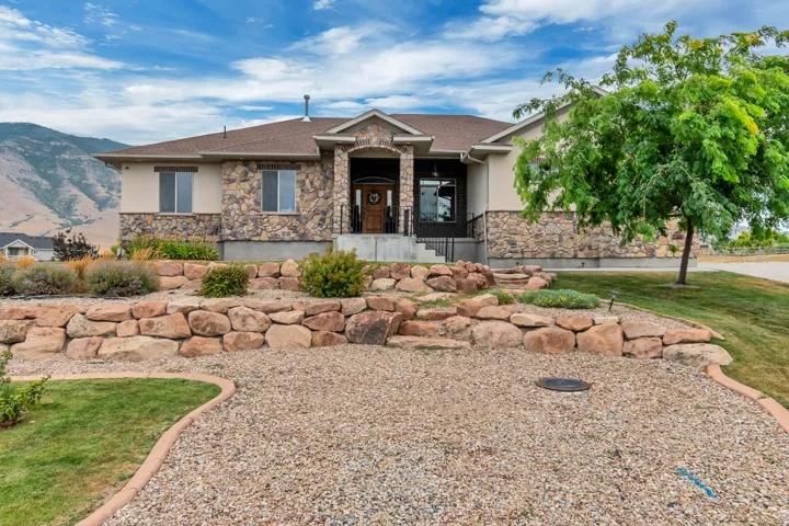 Stone and stucco exterior with a prominent arched entry, surrounded by tiered rock landscaping and a gravel driveway