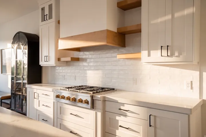 Gourmet kitchen featuring a built-in gas range, wood-finish floating shelves, and white shaker-style cabinetry with matte black hardware