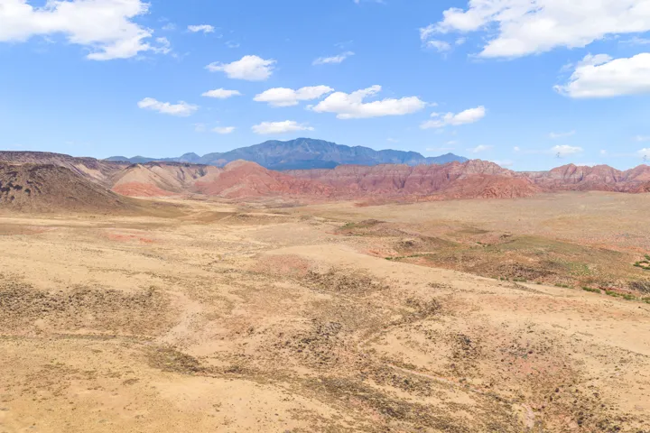 Expansive arid landscape featuring natural terrain and distant mountains under a blue sky with scattered clouds