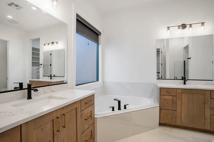 Bright bathroom featuring a corner soaking tub, dual wood-finish vanity cabinets with quartz countertops, and matte black fixtures
