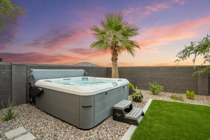 Outdoor spa set on a gravel bed with stepping stones, featuring a surrounding block wall and a mature palm tree