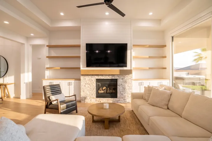 Living area featuring a stone-clad fireplace with a wood mantle, built-in shelving, wood-finish flooring, recessed lighting, and a ceiling fan