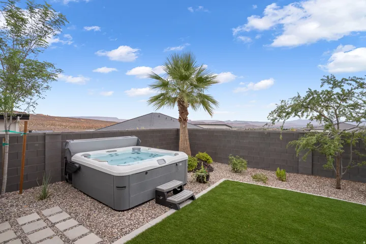 Outdoor spa with grey steps, surrounded by gravel and artificial turf