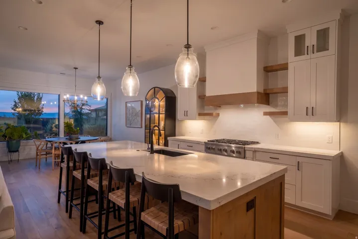 Spacious kitchen featuring an expansive island with seating, a built-in range, white shaker-style cabinetry, and wood-finish flooring