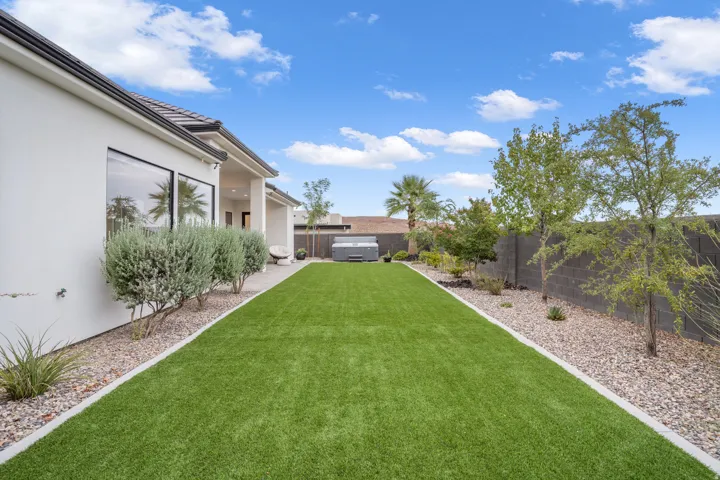 Expansive backyard featuring artificial turf, mature landscaping, and a built-in spa