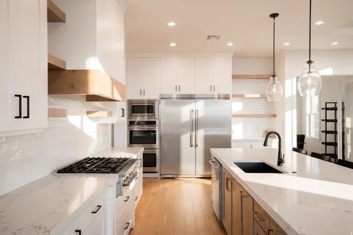 Gourmet kitchen featuring white shaker cabinetry, stainless steel appliances, a gas range with a wood-accented range hood, and a large island with a black sink and matte black faucet