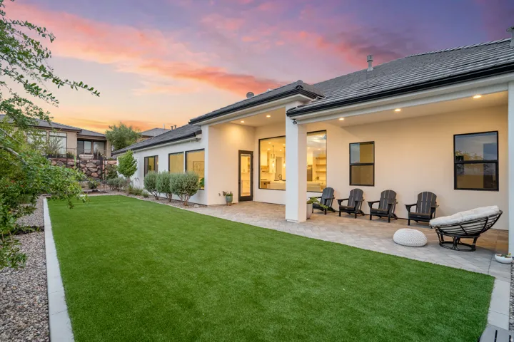 Expansive backyard featuring a large paved patio, artificial turf lawn, and mature landscaping