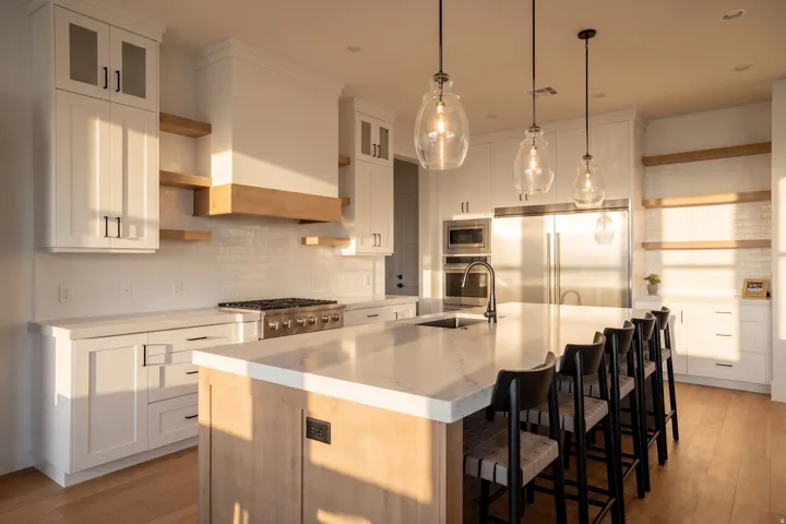 Open-concept kitchen featuring an expansive island with seating, stainless steel appliances, white shaker cabinetry, and wood-finish flooring