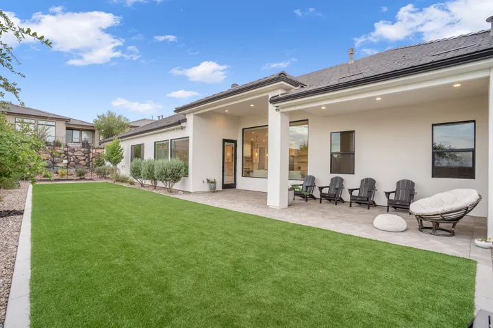 Expansive backyard featuring a manicured artificial turf lawn, a paved patio, and a covered outdoor living area with recessed lighting