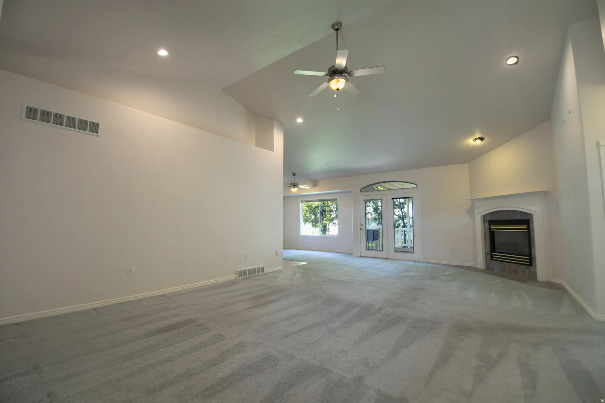 Vaulted ceilings with recessed lighting, ceiling fan, fireplace with mantel, and French doors