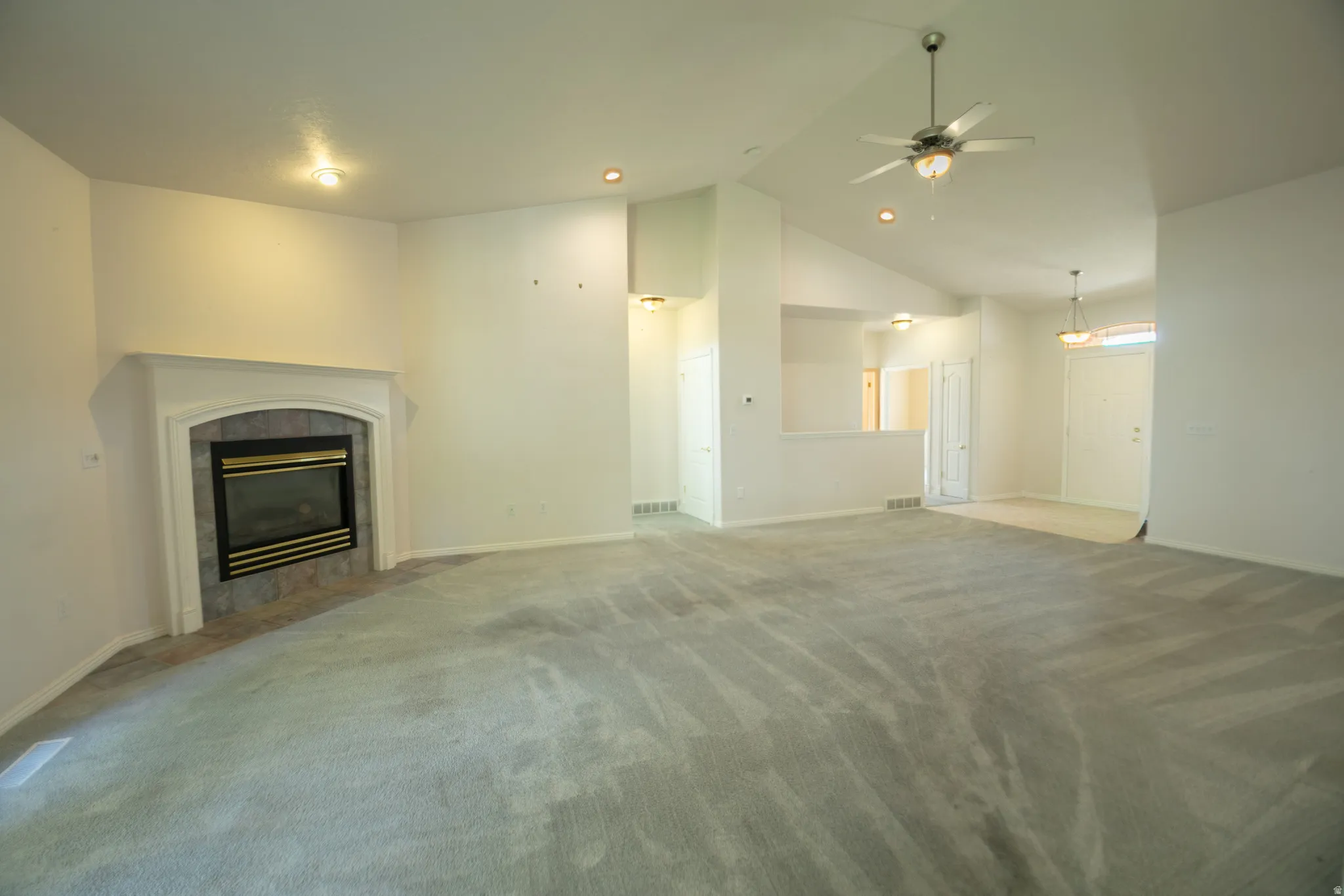 Carpeted living area featuring a fireplace with a tiled surround, vaulted ceiling, recessed lighting, and a ceiling fan