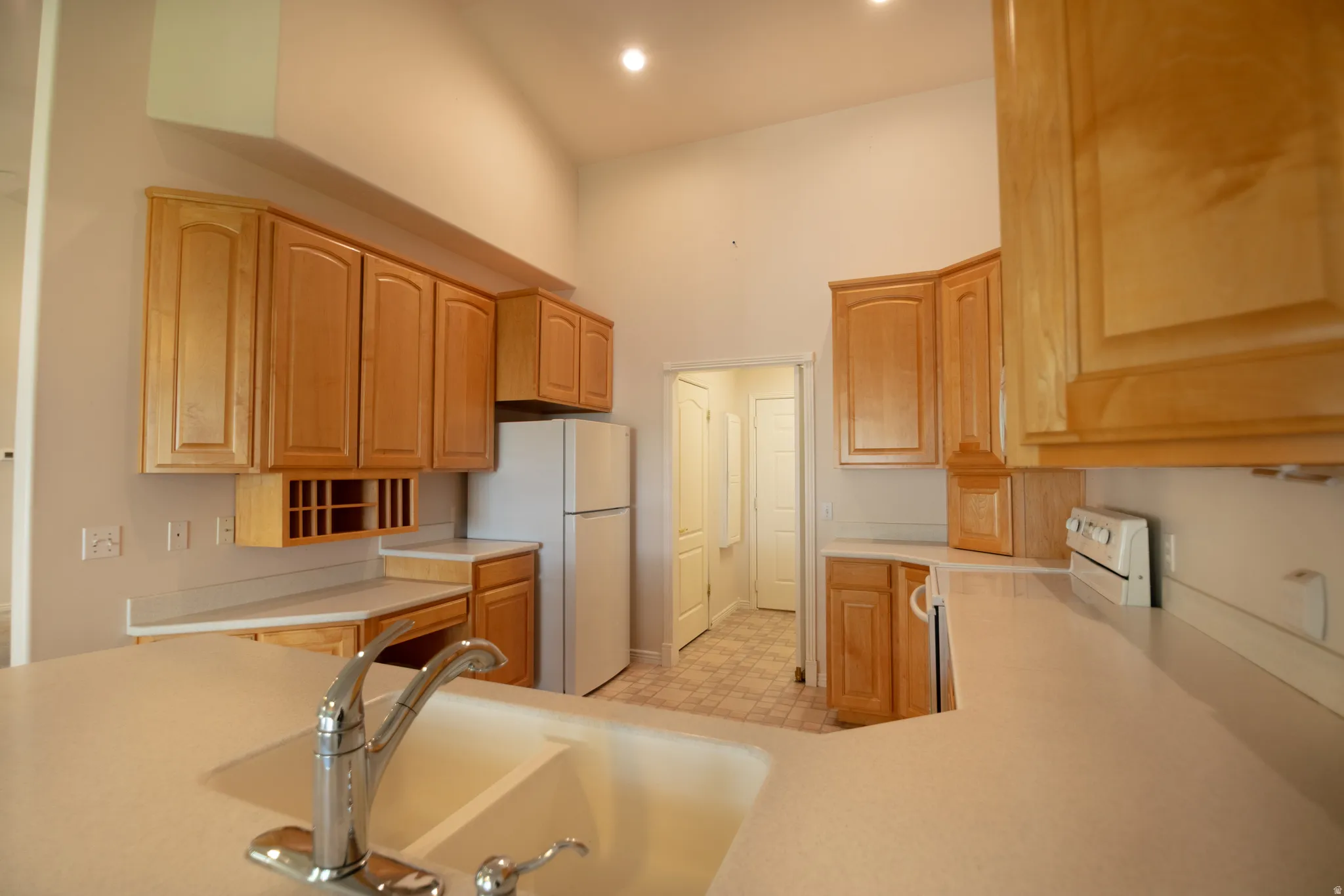 Vaulted ceiling kitchen featuring light wood cabinetry, a built-in wine rack, a stainless steel faucet, and recessed lighting