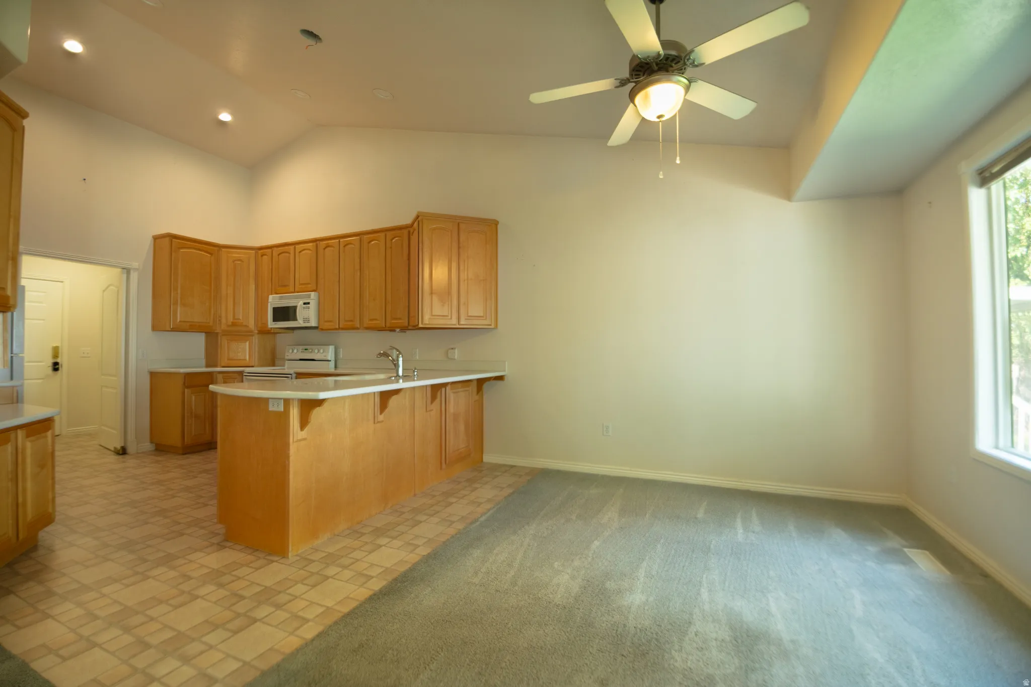Kitchen area featuring light wood cabinetry, a built-in microwave, and an integrated kitchen island with a breakfast bar