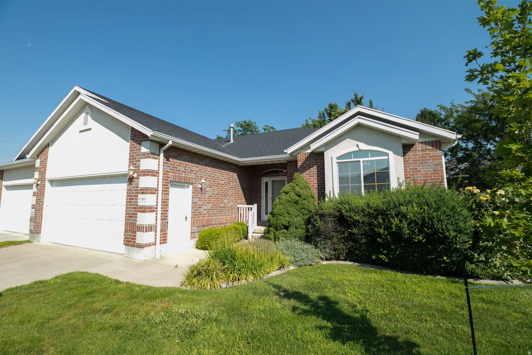 Brick facade with white trim, arched window, attached two-car garage, and established landscaping