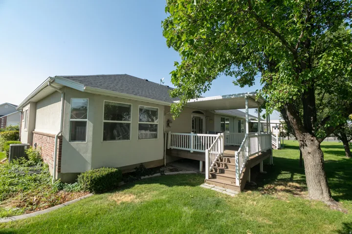 Expansive backyard with a covered deck, wood steps, white railings, and mature trees