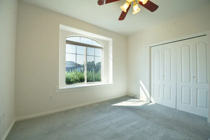 Arched window with grid pattern, neutral carpet flooring, bi-fold closet doors, and a ceiling fan with light fixture