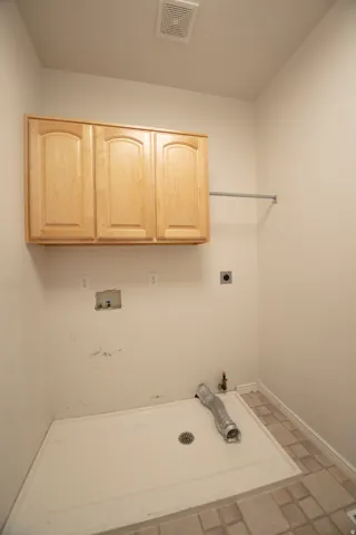 Wall-mounted cabinetry with light wood-finish doors, utility sink base, and durable tile flooring