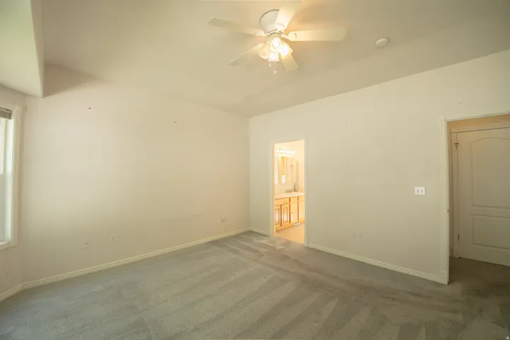 Spacious room featuring vaulted ceilings, light gray carpeting, and a ceiling fan with integrated lighting