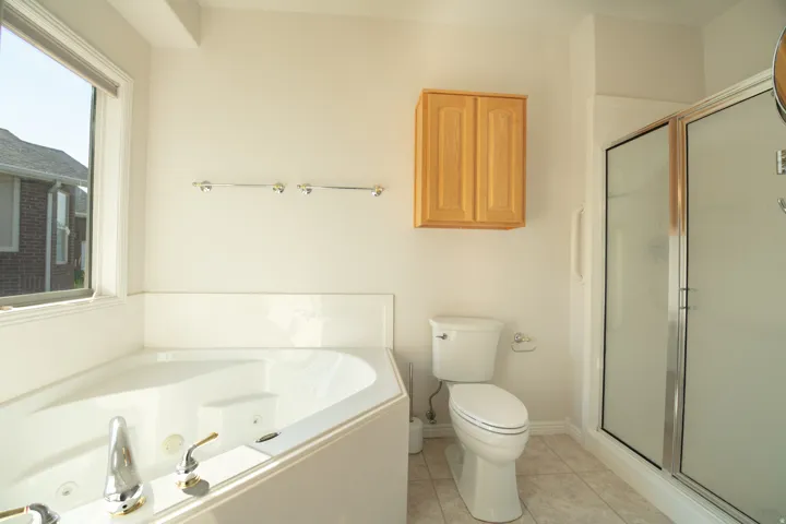 Corner soaking tub with polished chrome fixtures, white toilet, glass-enclosed shower, and wood-finish wall cabinet