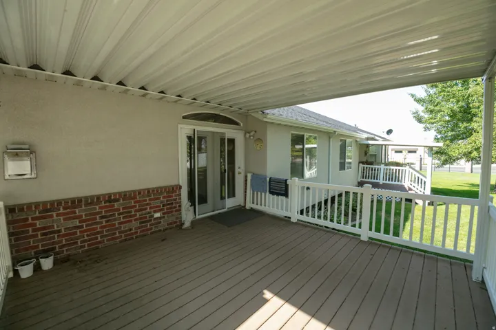 Covered patio featuring a composite deck, white railings, stucco siding, and brick accents