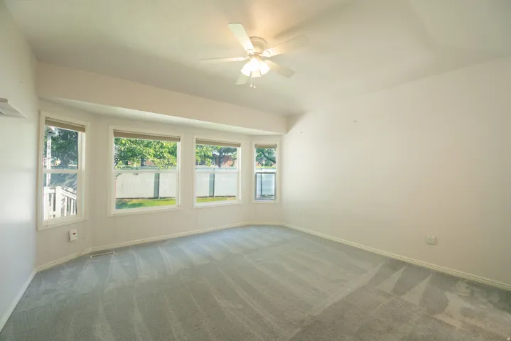 Bay window with multiple panes, ceiling fan, and light gray wall-to-wall carpeting