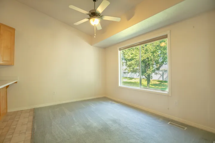 Vaulted ceiling, ceiling fan with integrated lighting, large window with white trim, light-toned carpeting, and built-in cabinetry with a light countertop