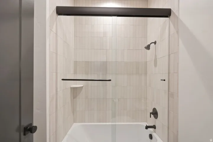 Bathtub and shower combination featuring floor-to-ceiling vertical tile, a frameless glass shower enclosure with dark bronze hardware, and coordinating dark bronze fixtures