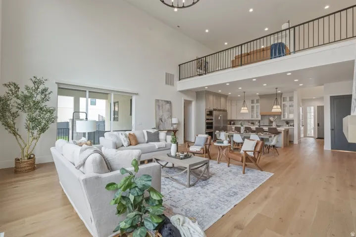Expansive open-concept living space featuring high ceilings, wood-finish flooring, a contemporary kitchen with an island, and a second-story loft area with a wrought iron railing