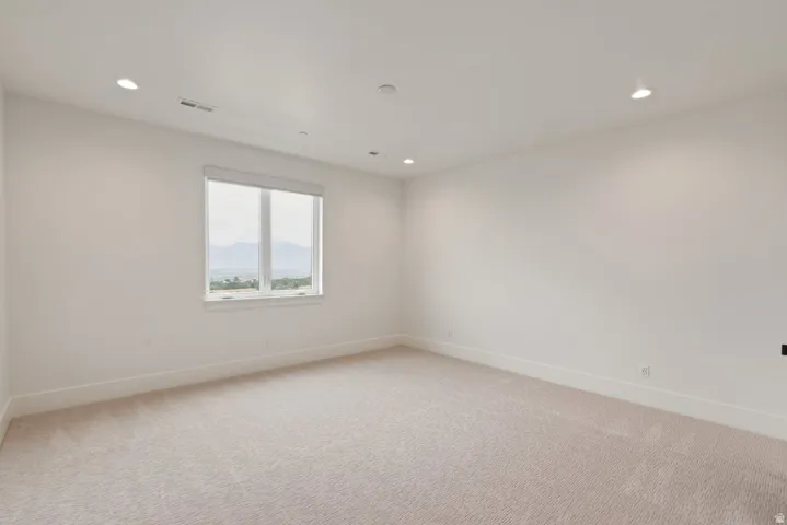 Spacious room featuring neutral carpeting, white walls, recessed ceiling lighting, and a large window offering distant mountain scenery