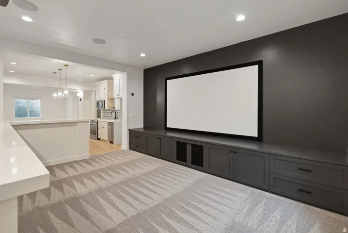 Media room featuring a large projection screen, extensive built-in cabinetry, recessed lighting, and patterned carpeting