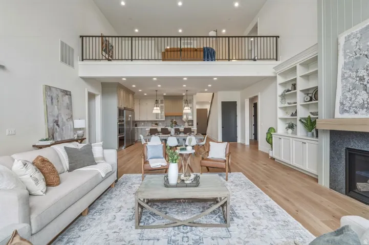 Two-story living area featuring wood-finish flooring, a built-in fireplace with a stone surround, and an open-concept kitchen