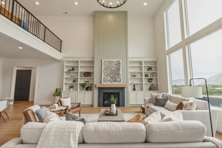 Spacious living area featuring a two-story ceiling, large format windows, a gas fireplace with a wood mantle, built-in shelving, and wood-finish flooring