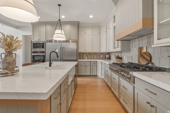 Gourmet kitchen featuring a substantial island with an integrated sink, light-toned cabinetry with brass hardware, a built-in stainless steel oven and microwave, a professional-grade gas range, and wood-finish flooring