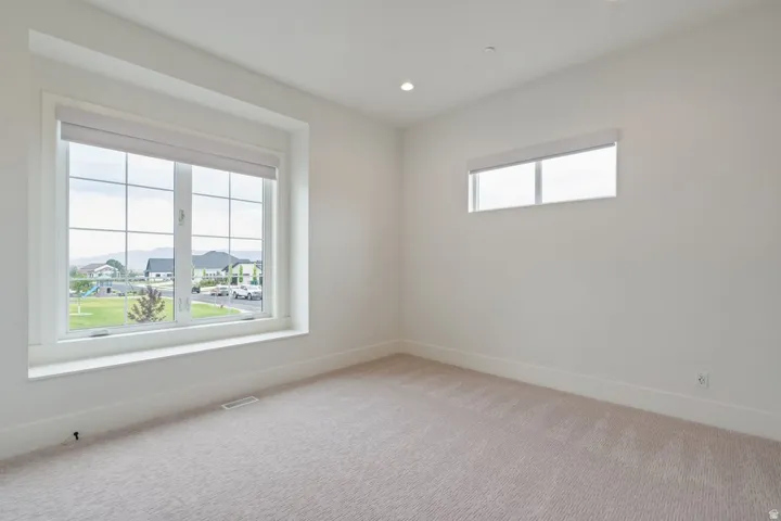 Bright room featuring a large picture window with grids, a second horizontal window, recessed lighting, neutral carpeting, and white baseboards