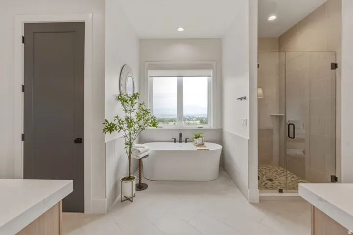 Freestanding soaking tub with a wall-mounted faucet, complemented by a glass-enclosed shower featuring a river rock floor and large format tile surround