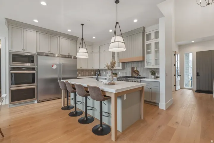 Gourmet kitchen featuring a large central island with seating, stainless steel appliances, light wood-finish flooring, recessed lighting, and elegant pendant fixtures