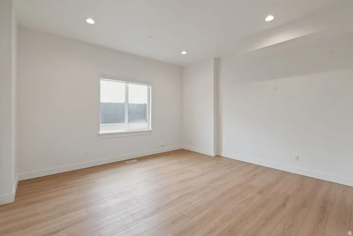 Spacious room featuring light wood-finish flooring, recessed lighting, white walls, and a large window with white trim