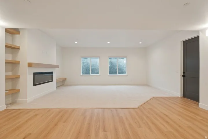 Spacious room featuring a contemporary fireplace with a light wood mantel, recessed lighting, and built-in shelving