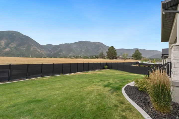 Expansive backyard featuring a manicured lawn, a privacy fence, and a decorative rock border