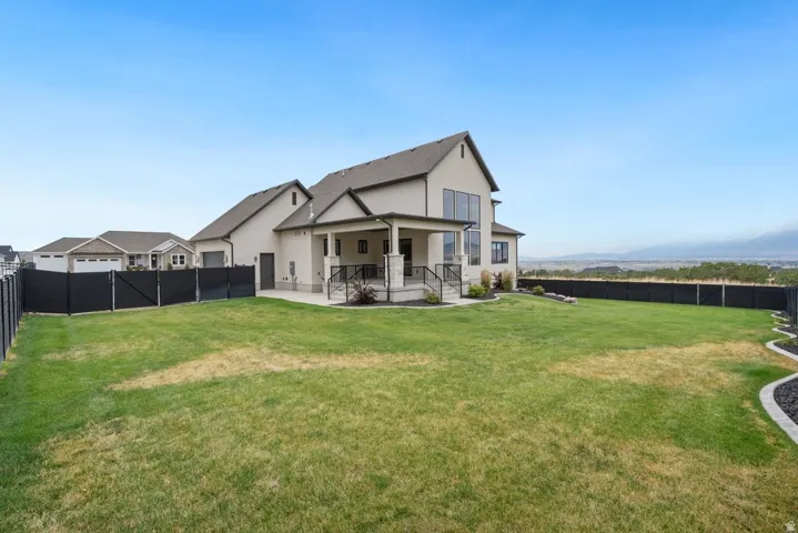 Spacious rear yard with a manicured lawn, full fencing, and a covered patio with railing