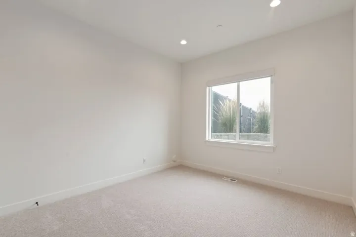 Spacious room featuring neutral carpet, recessed lighting, and a large window with white trim